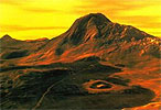 Вулканическая деятельность на Венере, крупнейший вулкан Венеры — гора Маат возвышается на 8 км над своим подножьем и на 11 км — над средним уровнем планеты. Диаметр основания этого вулкана — 600 км. Только здесь найдены признаки недавней активности — вершина горы покрыта темным веществом с уникальными характеристиками, которых нет ни у одного из сотен вулканов Венеры. На переднем плане — свежий лавовый поток, в центре — кратер Пископия диаметром 26 км, узкая светлая линия — тектонический разлом, указывающий, что в этой области были землетрясения. На горизонте — еще один крупный вулкан высотой 7 км — гора Уззы.